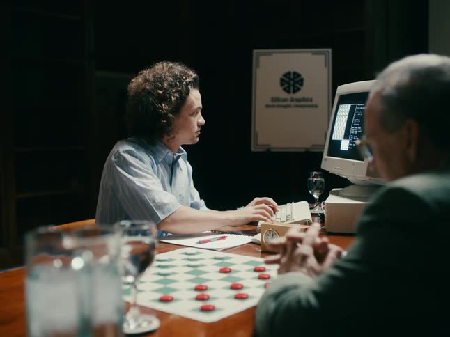 Two men play checkers and one records the moves on an old computer