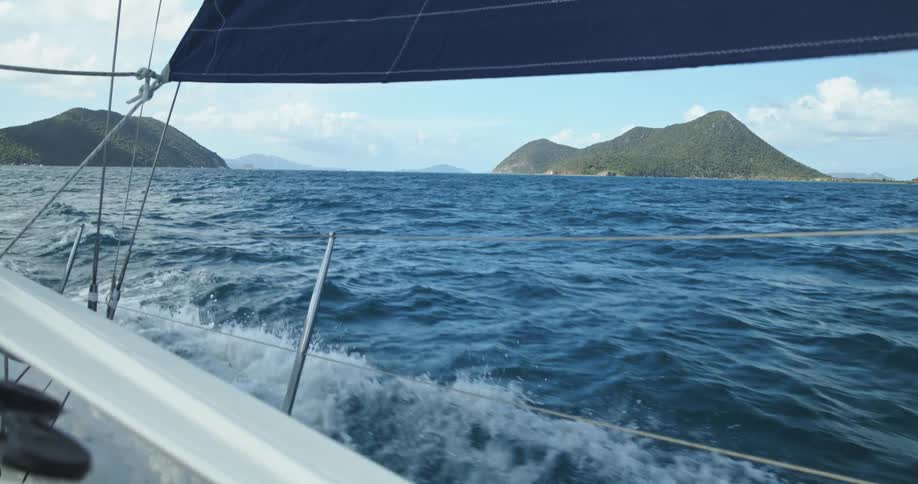 Sailboat moves quickly through water a distance from islands