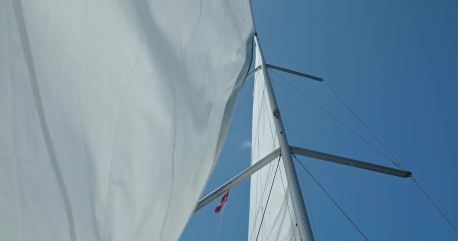 The wind blows the sail of a sailboat under a clear blue sky
