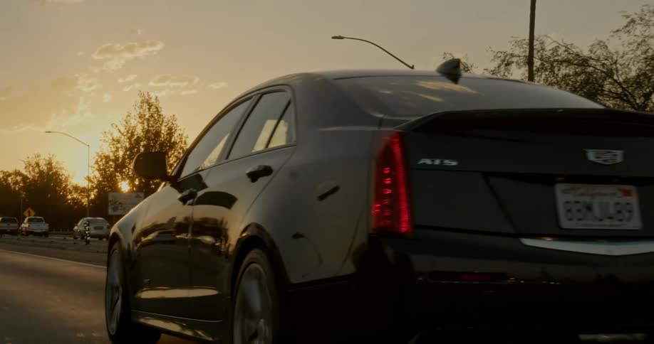 Dark gray cadillac ats pulling into frame driving on freeway toward sunset