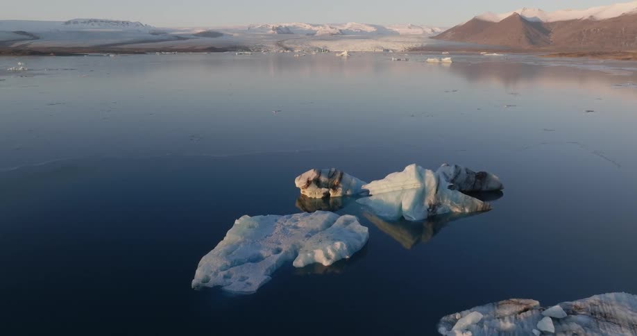 Aerial view of small icebergs floating in the ocean in front of a distant glacier at evening