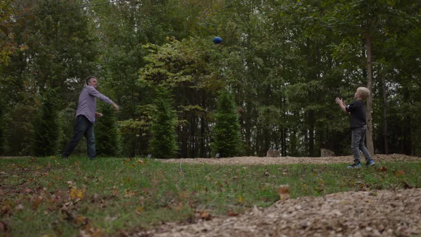 Father and son tossing a football on a grassy lawn