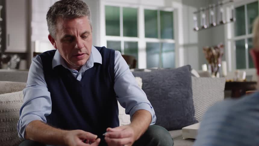 A father and son are sitting in a living room while working a jigsaw puzzle together