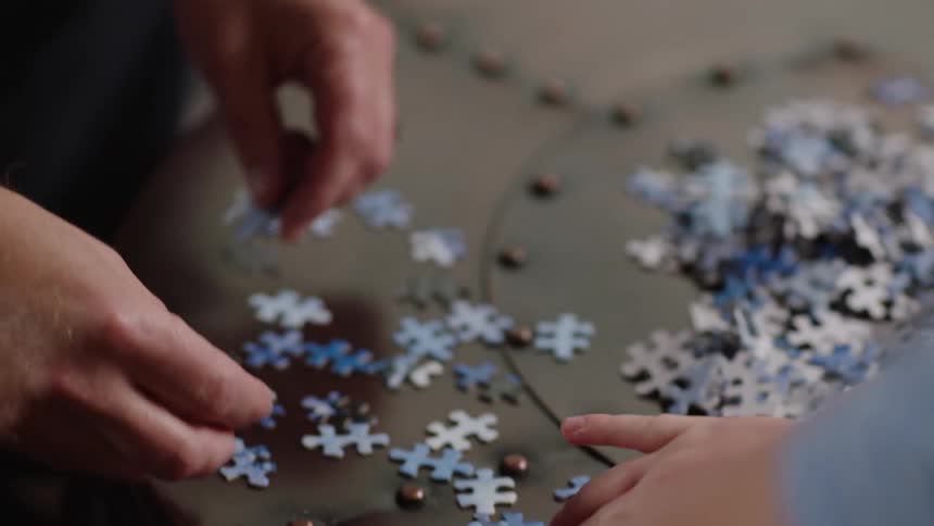 Father and son are working on putting together a large jigsaw puzzle on a table in a living room in the daytime