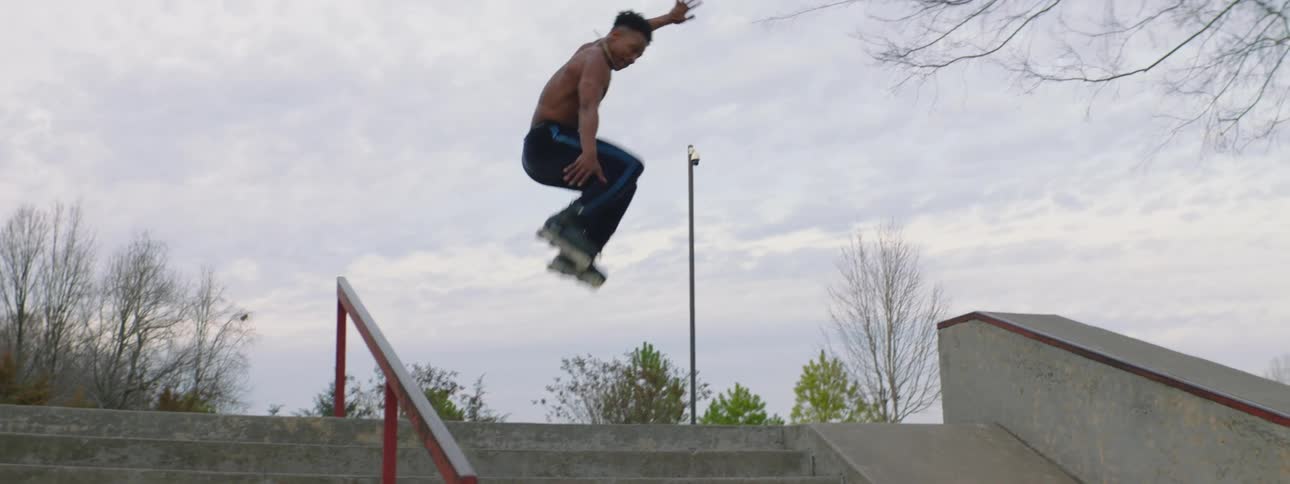 Inline skater jumps through air over outdoor staircase under an overcast sky