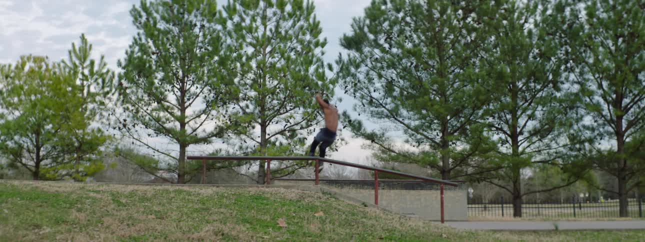 Young muscular shirtless man wearing roller skates jumps down a ramp on a park