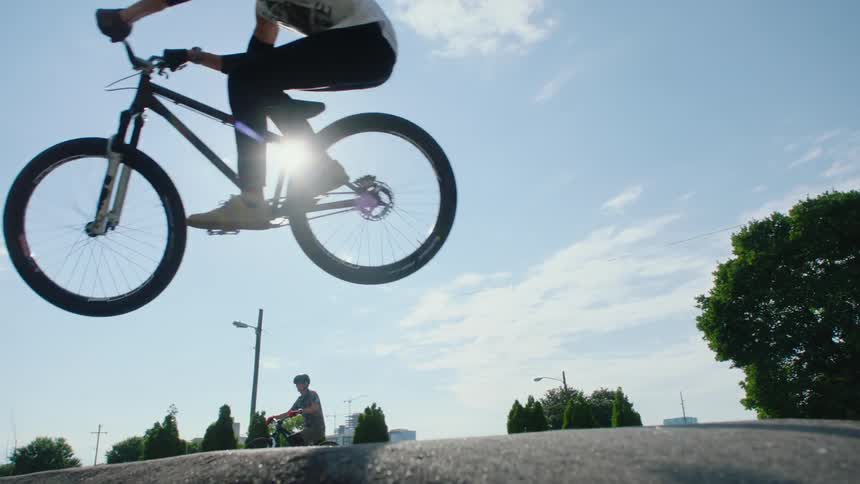 Young person jumps over a concrete structure on a park with a motocross bicycle