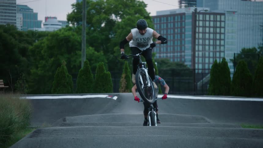 Two cyclists jumping and driving motorcross bicycles on a beautiful small track on a park