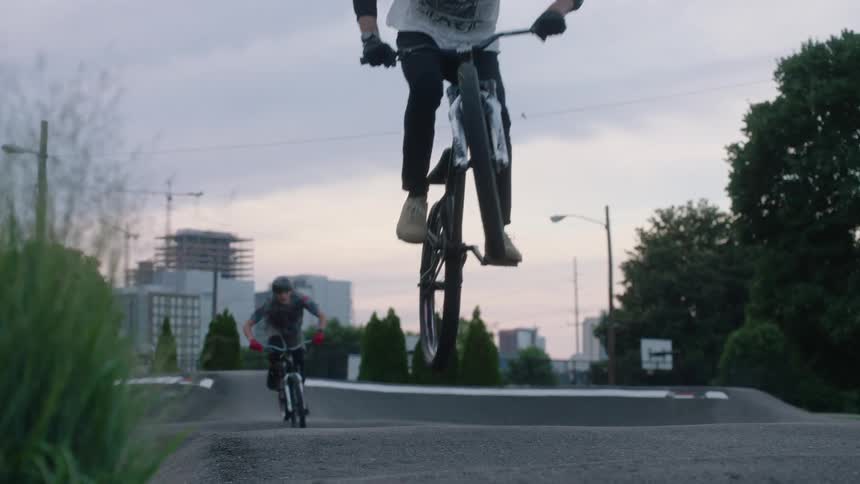 Two cyclists ride bmx course with buildings in the background