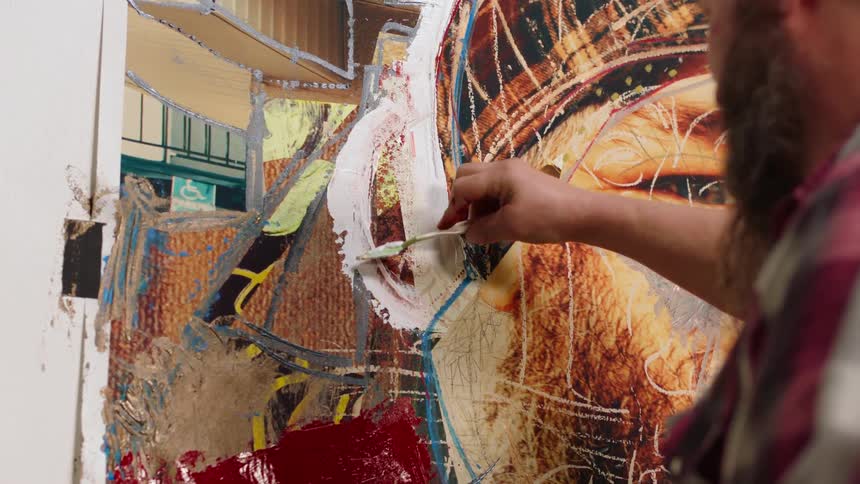 Bearded male artist applies layer of paint to artwork using small palette knife