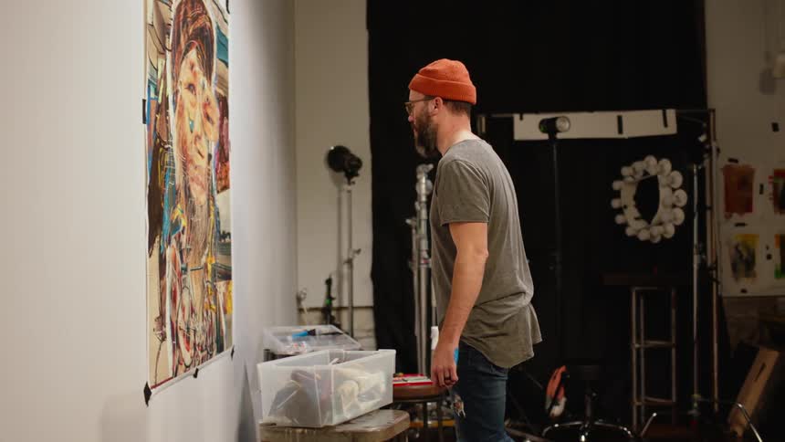 A man is standing near a wall as he paints a mural and he steps back to take a look