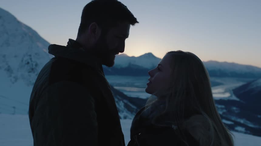 Two people look at each other smiling near mountains