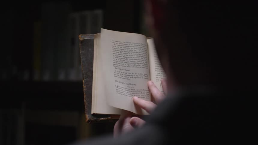 Man reads a book next to a bookshelf