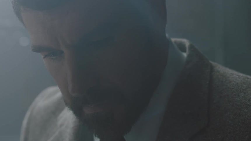 A bearded man in a suit looks down