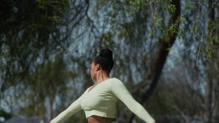 A female dancer in a crop top dancing outside beneath a large tree