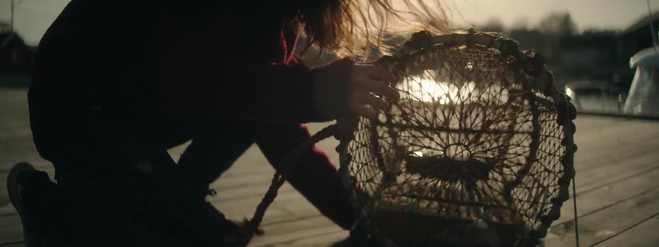 A woman kneeling down messing with a net as the sun shines down