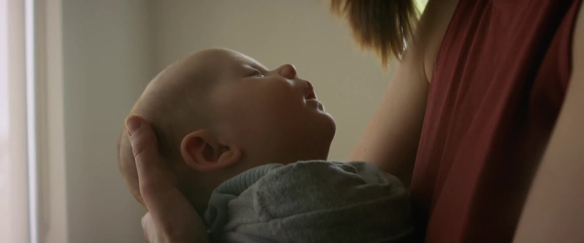 A woman leans down while cradling her baby in her arms