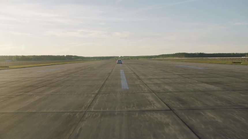 Car drives along broad runway trough fields toward forest