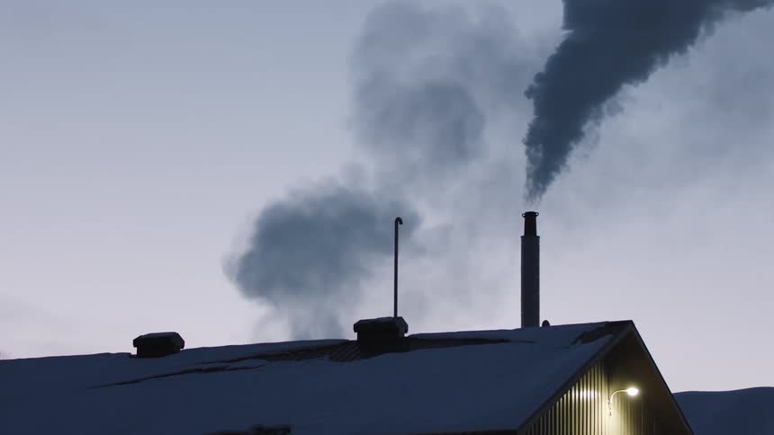 A snowy roof with chimneys that have smoke rolling out of them