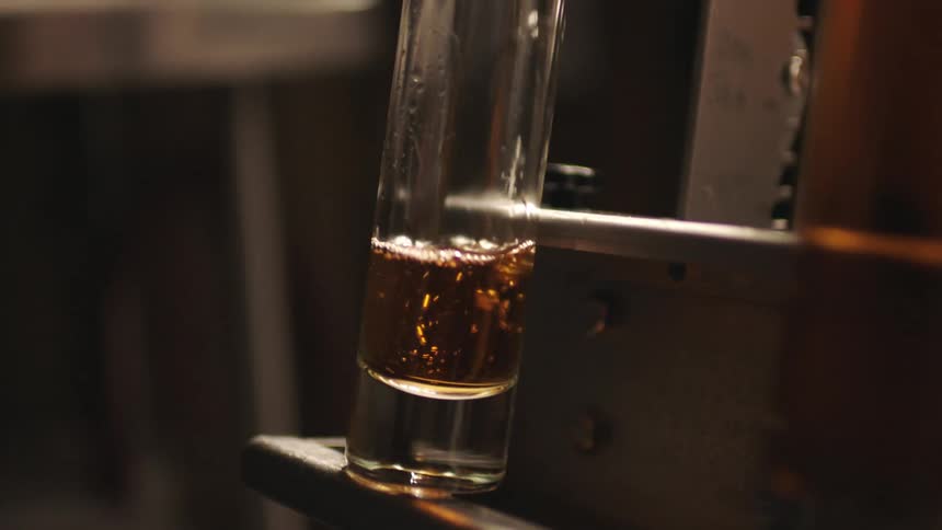 Man inserts a bottle into the bottle filling machine which fills it with a yellowish spirit