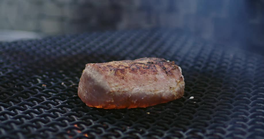 Man uses tongs to flip steak over on grill