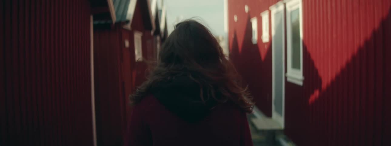A woman walking between red buildings
