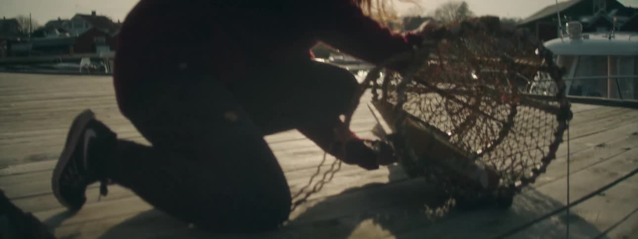 A woman bent over tending to a net on a boat dock