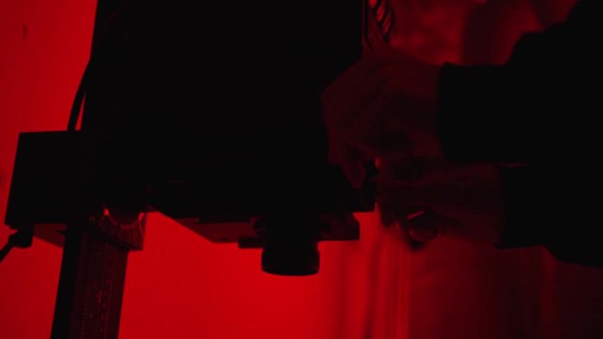 Close up of the silhouette of a person inserting film into enlarger inside a dark room