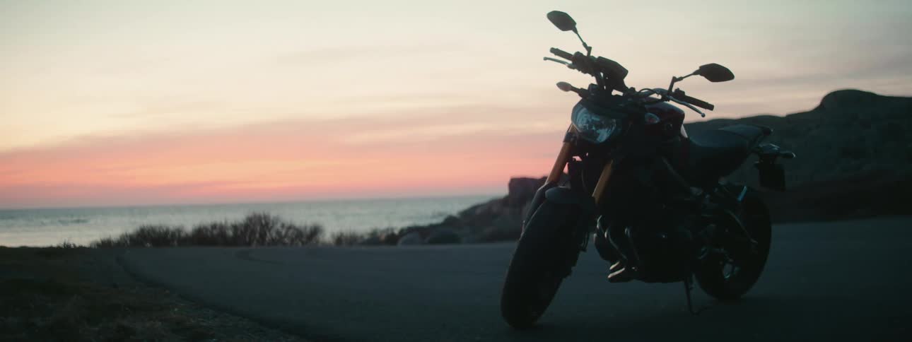 A motorcycle is parked on a road overlooking the ocean at sunset