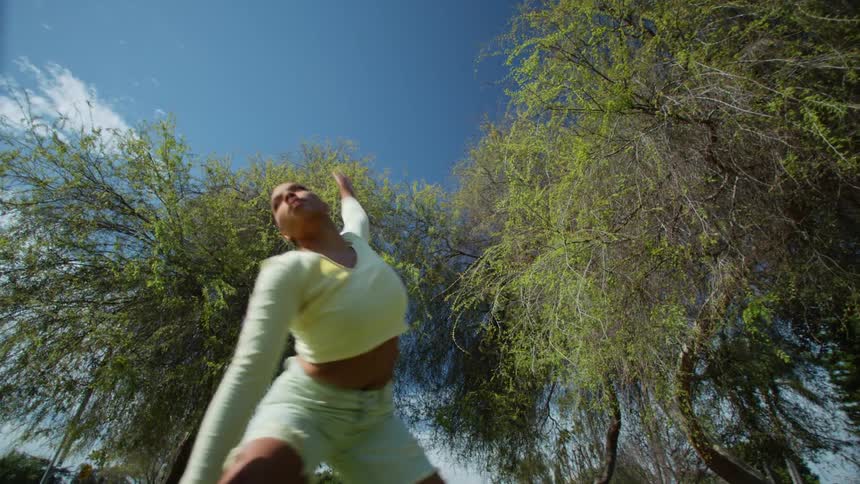 A woman moving her arms around and dancing under trees