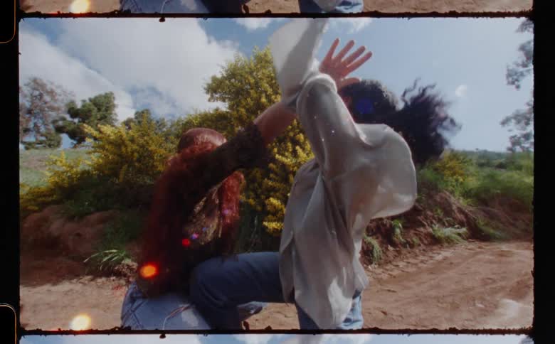Two teenage girls dance together outside on a dirt path