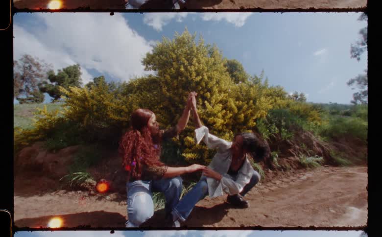 Two woman are performing an interpretive dance together on the turn of a dirt bike track in front of a dirt mound