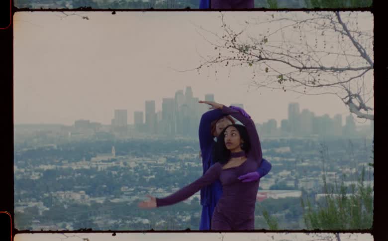 Women wearing purple and blue dresses dance against the city skyline