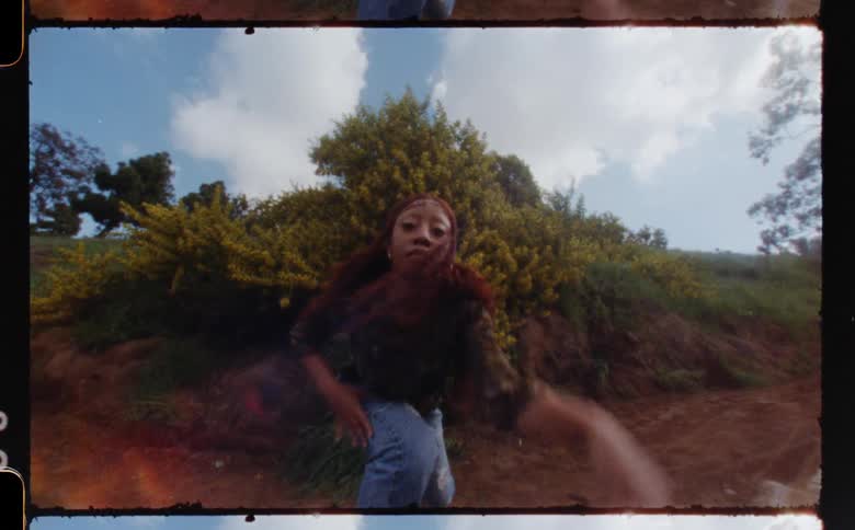 A woman dancing and moving abruptly outside in front of a yellow bush
