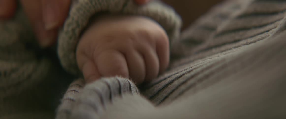 Nursing baby clutches moms sweater while mom holds babys arm