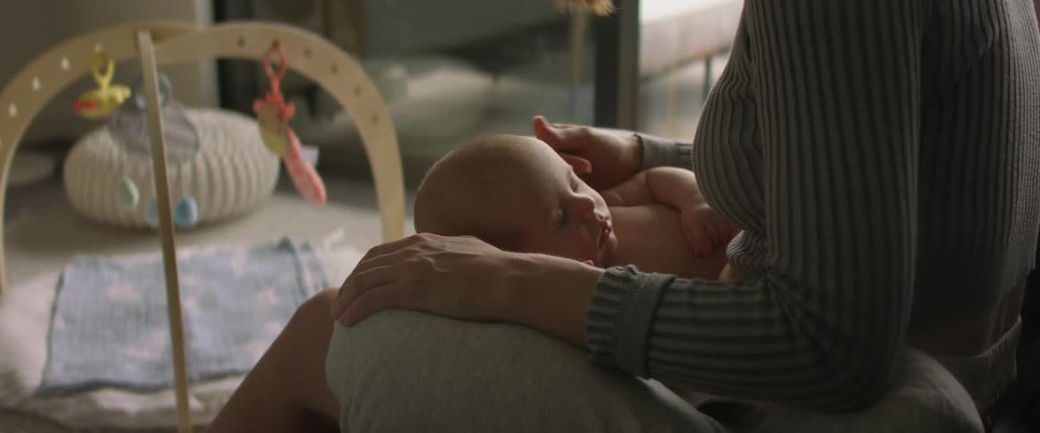 Newborn baby sleeping on the lap of his mother at home