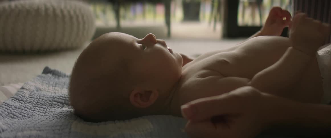 Happy baby lying on baby blanket while mother plays with cheeks