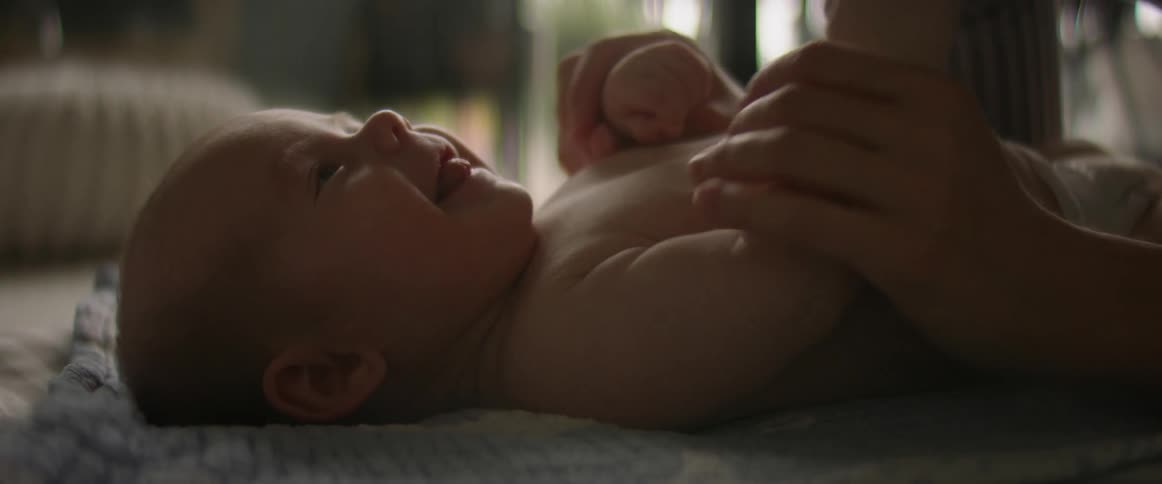 A baby lays on the floor while an adult plays and makes the baby laugh and smile