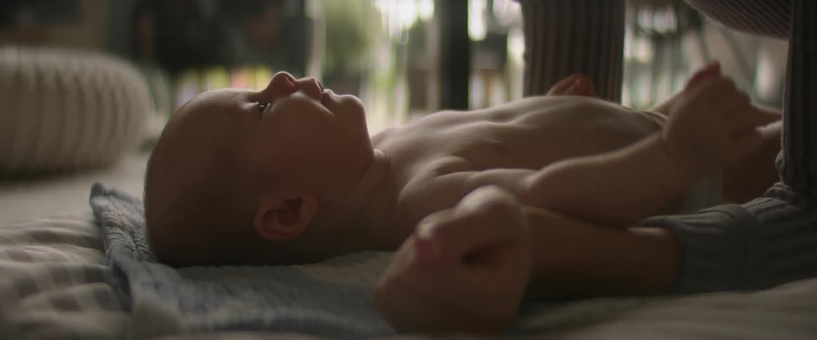 A baby in a diaper on the floor as an adult leans over the baby