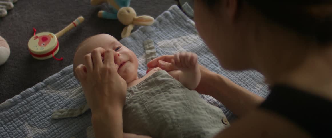 A newborn baby lays on a baby blanket as his mother touches his face lovingly