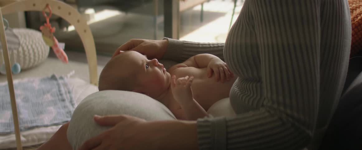 Mother sits on couch and caresses head of child lying on pillow in her lap