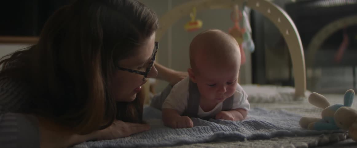 A woman is lying on a blanket next to her baby as they move and put their face in the blanket