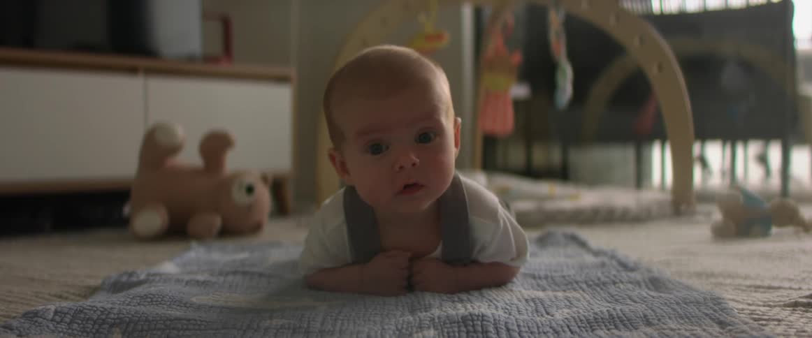 Adorable baby looking around laying on tummy on blanket on the floor