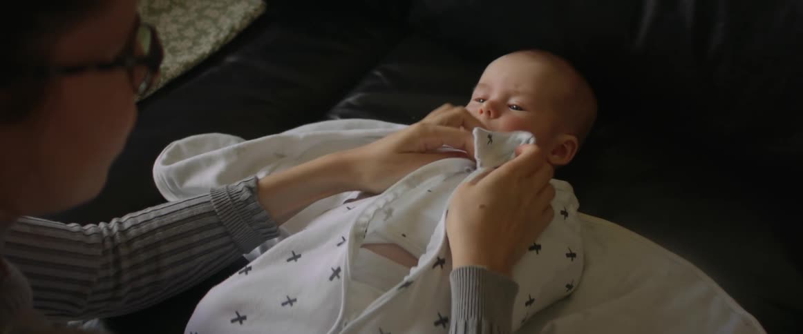 Mom swaddling infant baby lying on back