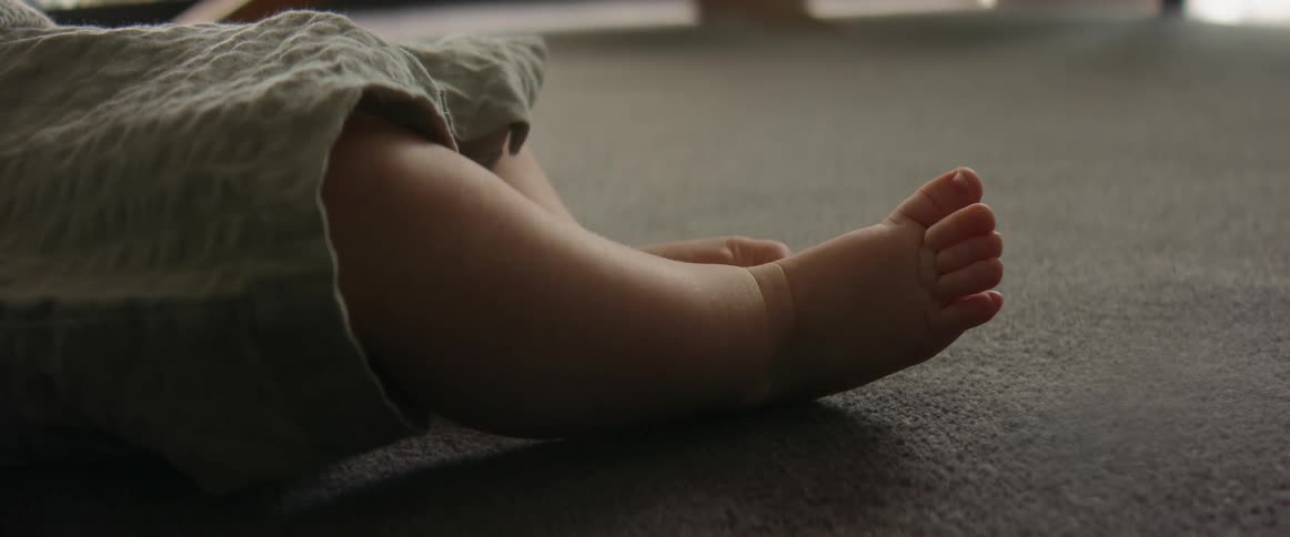 A baby is lying on the floor moving their feet and toes