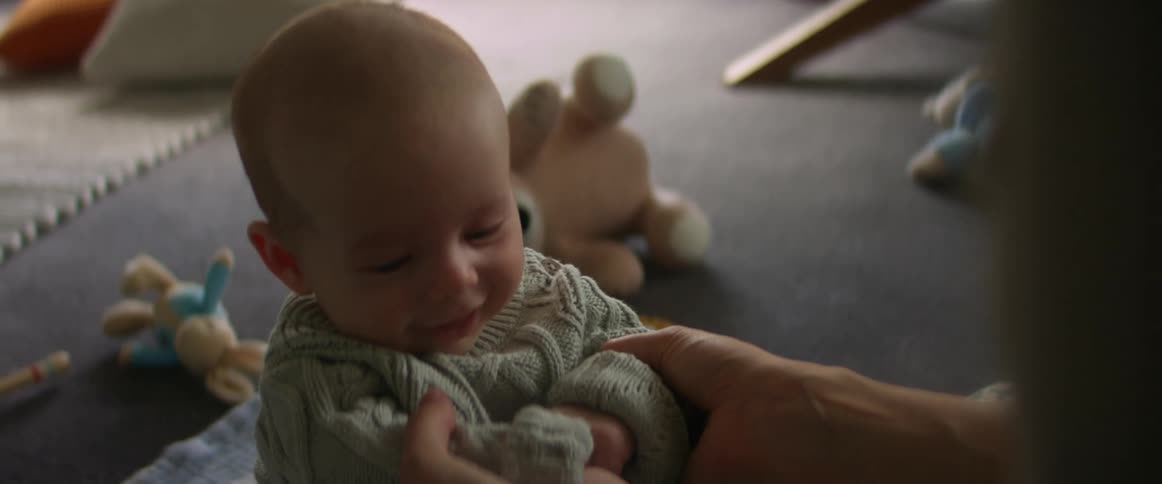 Mother holds baby son with sweater looking around in the living room