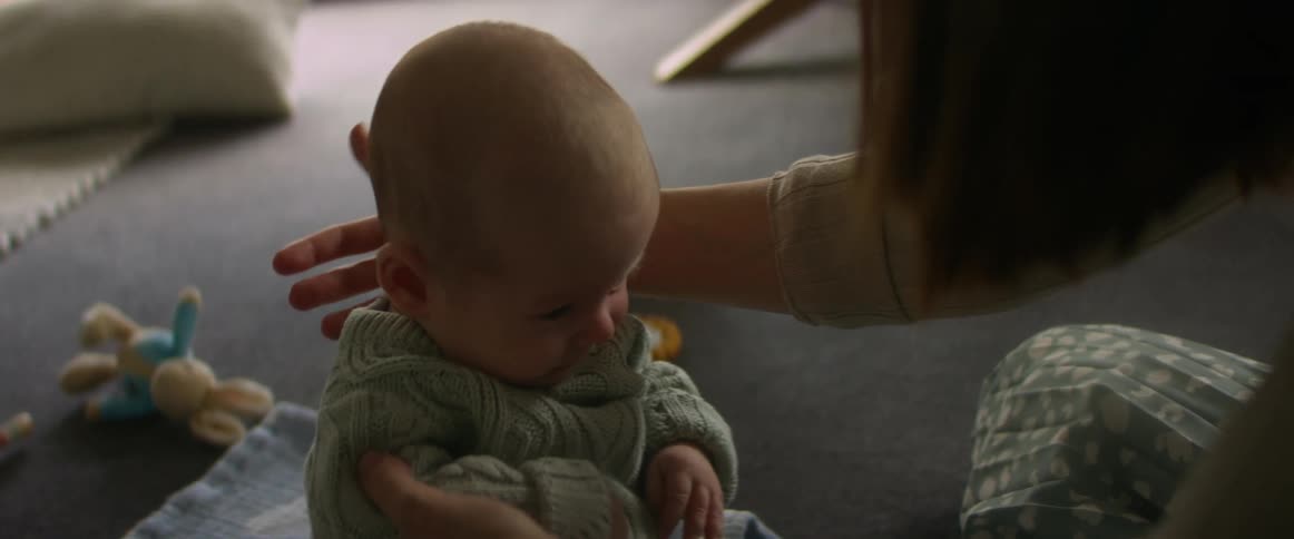 A mother holding up a baby sitting on the floor