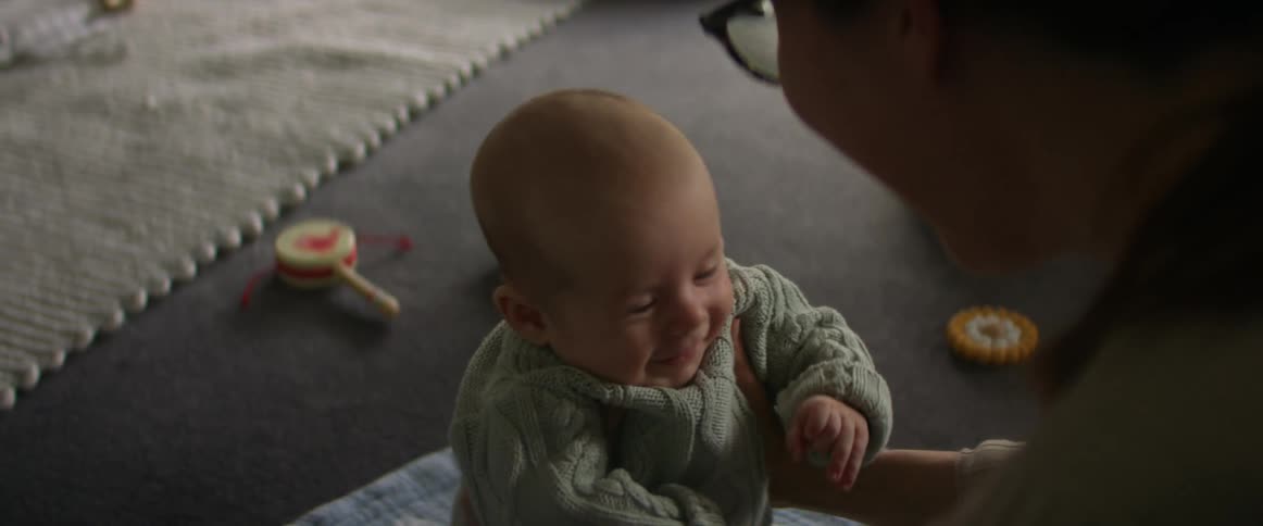 Mother with glasses holds baby son and looks into his smiling son in the living room