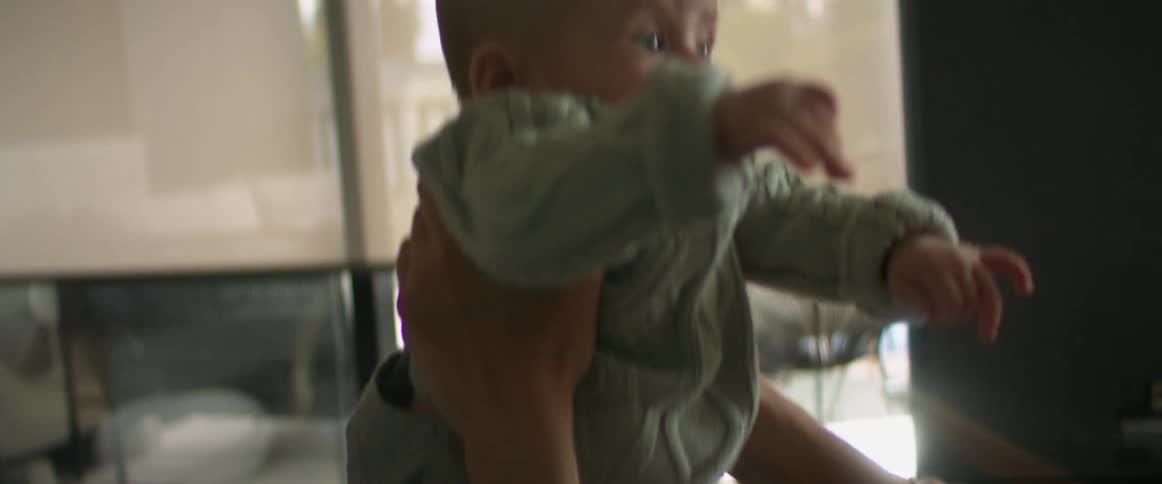 A woman picks her baby up and down while playing on the floor
