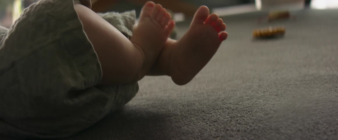 A baby boys legs are movin gup and down and he is bending his knees and and curling is toes slightly as he places one foot on the opposite leg then switches and does the opposite foot on the opposite leg